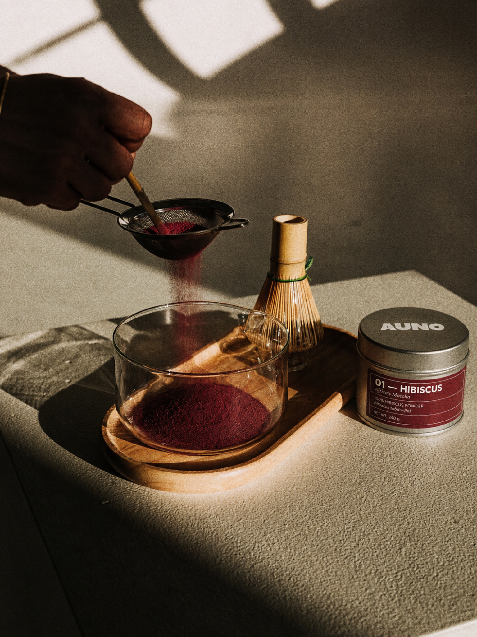 Sifting AUNO hibiscus powder into a bowl beside a whisk